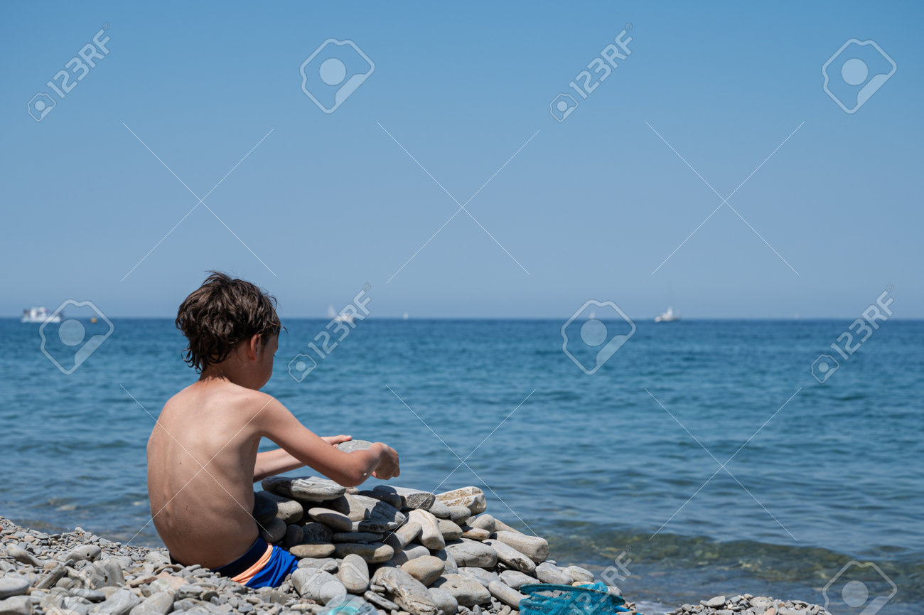 Child playing with rock on the beach on a beautiful sunny day. - 170456328 Child playing with rock on the beach on a beautiful sunny day. - 170456328