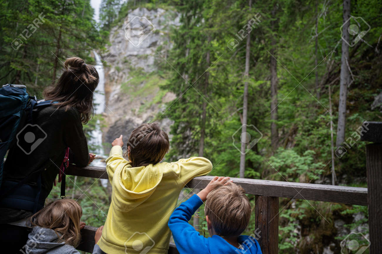 View from behind of a young mother with three children looking at a beautiful waterfall in green summer nature. - 171619924 View from behind of a young mother with three children looking at a beautiful waterfall in green summer nature. - 171619924