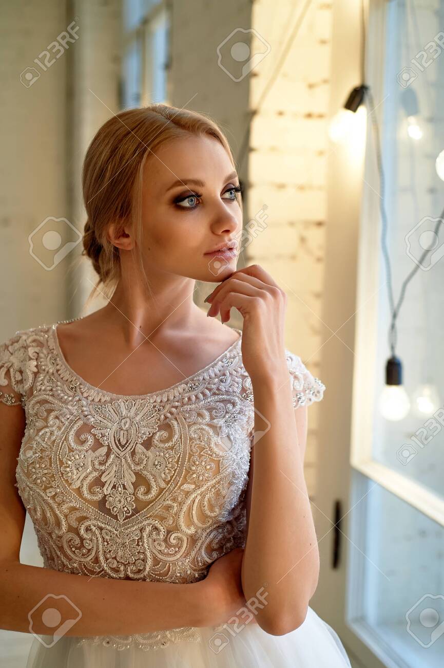 The Bride In A Lace Dress, With A Bunch. Restrained Elegance. Blonde.  Looking Out The Window Stock Photo, Picture and Royalty Free Image. Image  122584336.