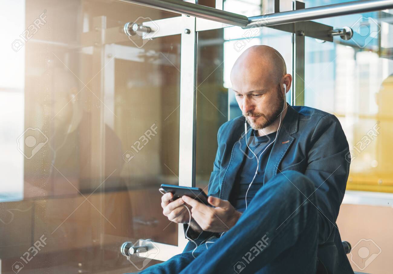Handsome bald bearded man in suit using mobile phone at airport lounge - 150607133 Handsome bald bearded man in suit using mobile phone at airport lounge - 150607133