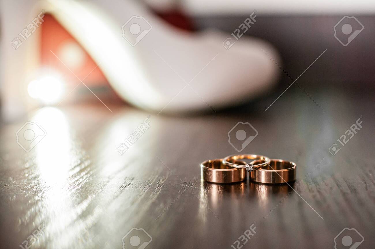 Three gold wedding rings and white high heel shoe on the table - 146237000 Three gold wedding rings and white high heel shoe on the table - 146237000