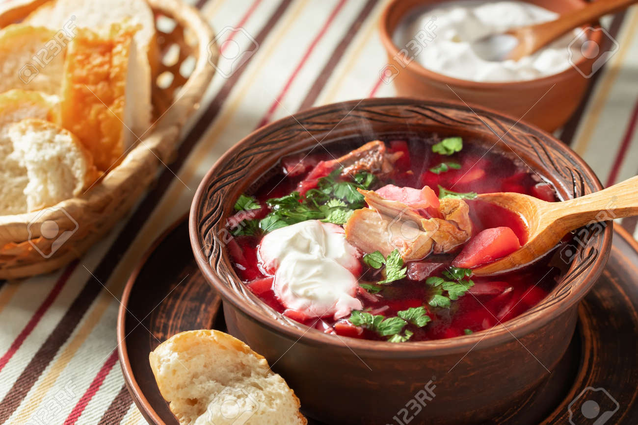 Freshly cooked hot homemade borscht - traditional dish of Russian and Ukrainian cuisine in earthenware dishes with bacon, bread, sour cream and garlic - 170577188 Freshly cooked hot homemade borscht - traditional dish of Russian and Ukrainian cuisine in earthenware dishes with bacon, bread, sour cream and garlic - 170577188