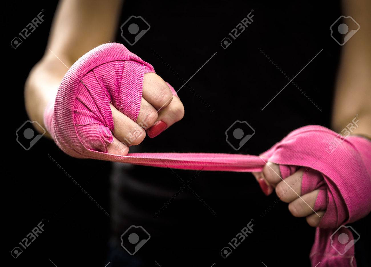 Woman is wrapping hands with pink boxing wraps. Isolated on black with red nails. Strong hand and fist, ready for fight and active exercise - 51071677 Woman is wrapping hands with pink boxing wraps. Isolated on black with red nails. Strong hand and fist, ready for fight and active exercise - 51071677