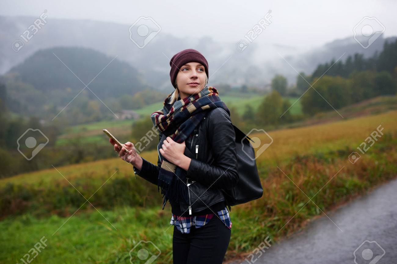 トレンディな女性はリュックサック ウォーキング ツアー中に携帯電話のテキスト メッセージを待っている美しい女性観光客 山で興味深い場所を捜している間彼女の携帯電話の信号をキャッチします の写真素材 画像素材 Image