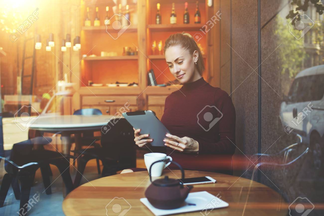 快適なカフェ モダンなコーヒー ショップに座ってタッチ パッドでかなり女性フリーランス作品の中で女性読書電子書籍デジタル タブレットの昼食時に上の窓を破るを表示します の写真素材 画像素材 Image