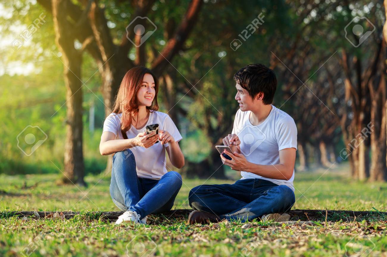 couple using mobile phone and talking in the park - 95604572 couple using mobile phone and talking in the park - 95604572