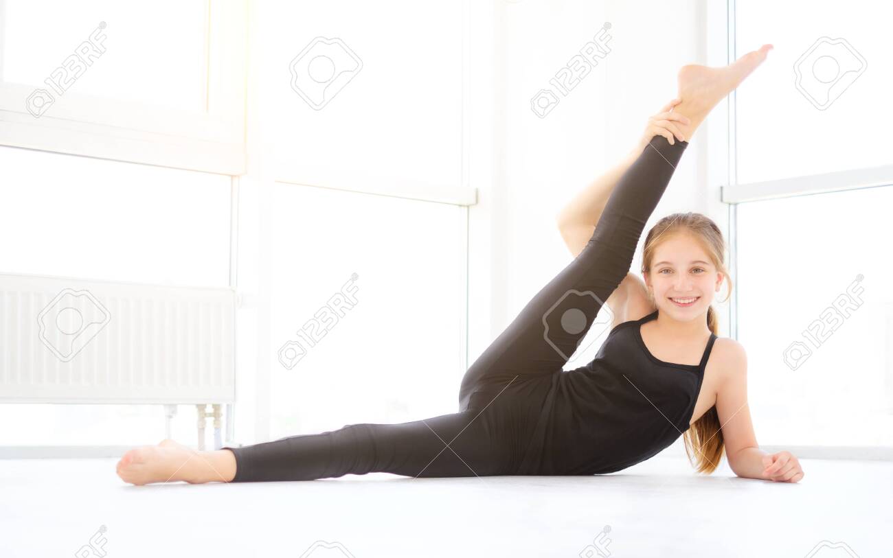 Pretty Young girl dancer doing stretching legs in white room - 143203306 Pretty Young girl dancer doing stretching legs in white room - 143203306