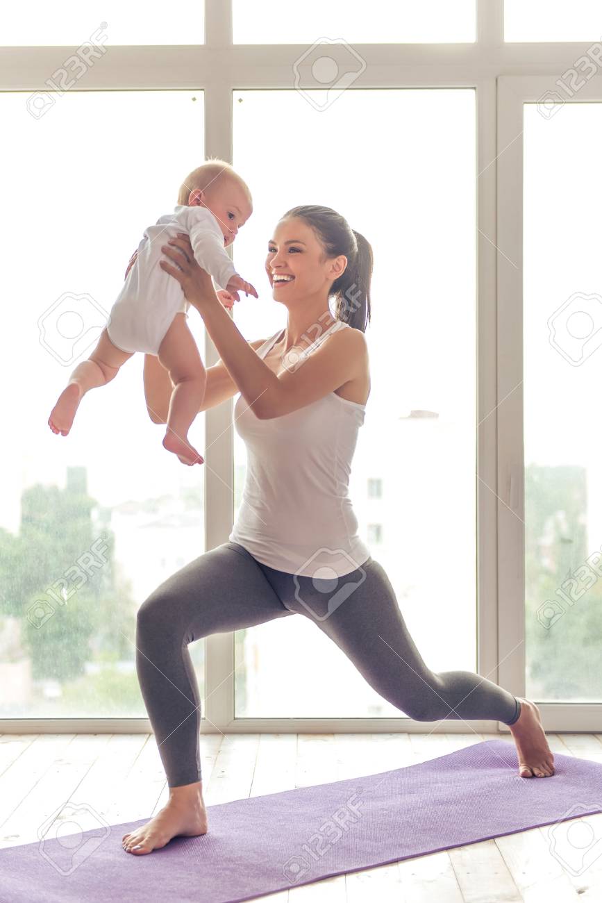 Belle Jeune Maman Dans Les Vetements De Sport Est Souriant Tout En Faisant Du Yoga Avec Son Charmant Petit Bebe Sur Un Tapis Contre La Fenetre Banque D Images Et Photos Libres De