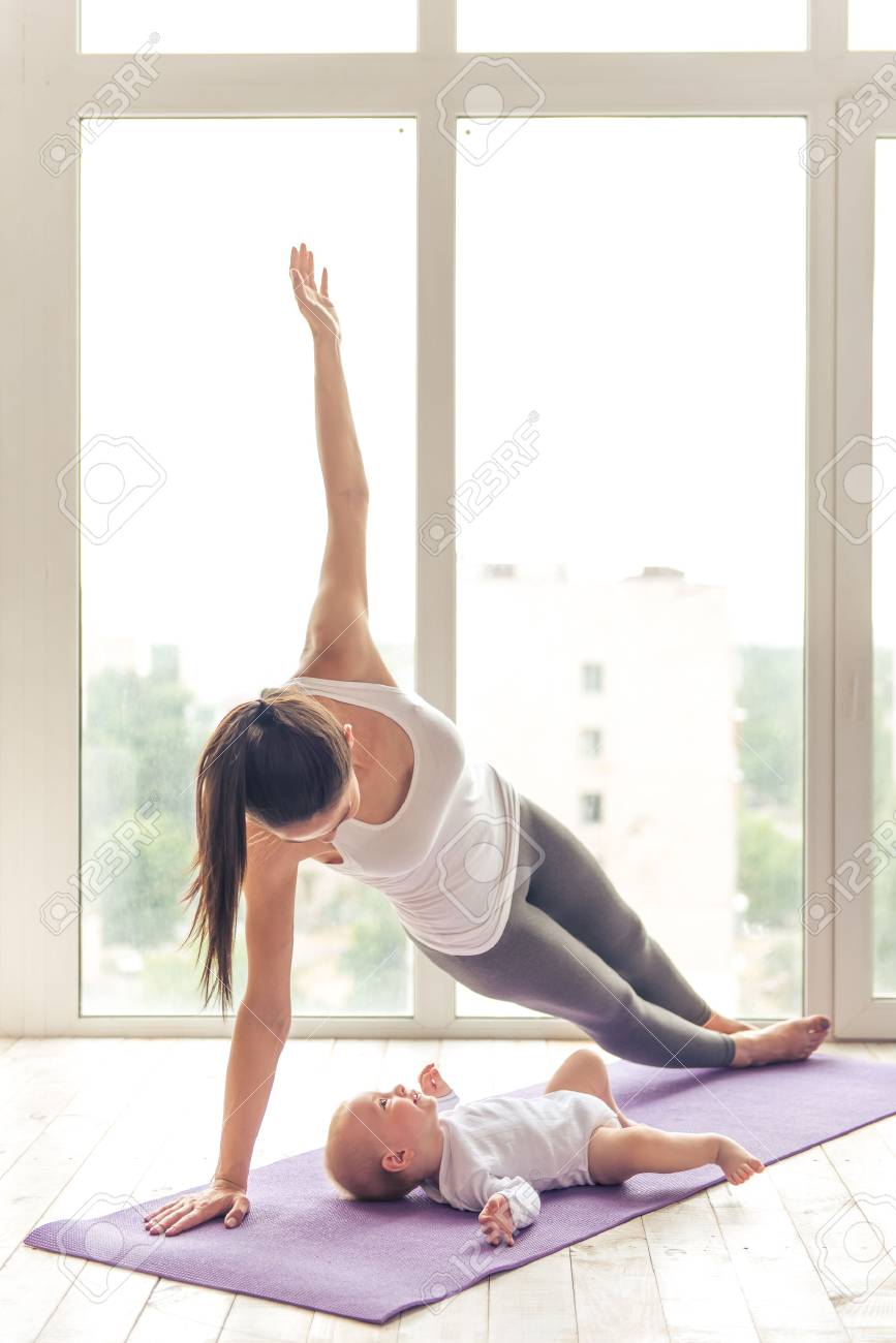 Belle Jeune Maman Dans Les Vetements De Sport Est Souriant Tout En Faisant Du Yoga Avec Son Charmant Petit Bebe Sur Un Tapis Contre La Fenetre Banque D Images Et Photos Libres De