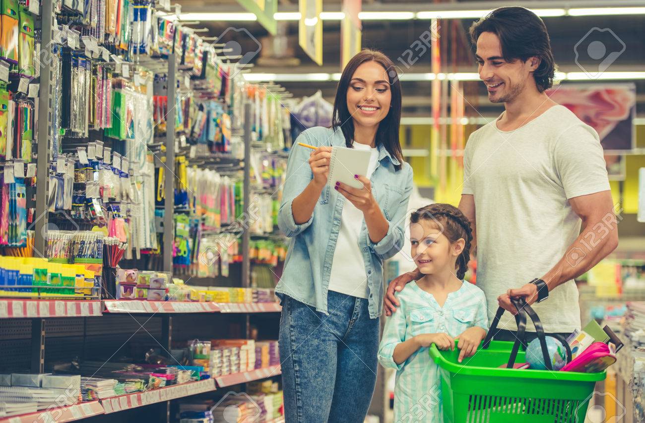 Beautiful young parents and their cute little daughter are smiling while choosing school stationery in the supermarket. Mom is making notes in the list - 62528285 Beautiful young parents and their cute little daughter are smiling while choosing school stationery in the supermarket. Mom is making notes in the list - 62528285
