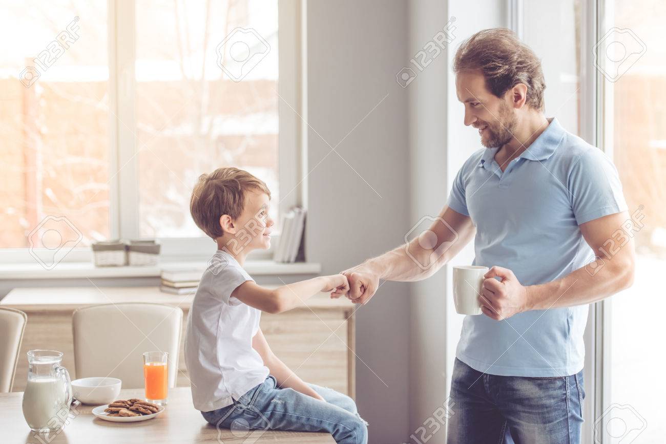 Father and son are giving five and smiling while having a snack in kitchen - 66198012 Father and son are giving five and smiling while having a snack in kitchen - 66198012