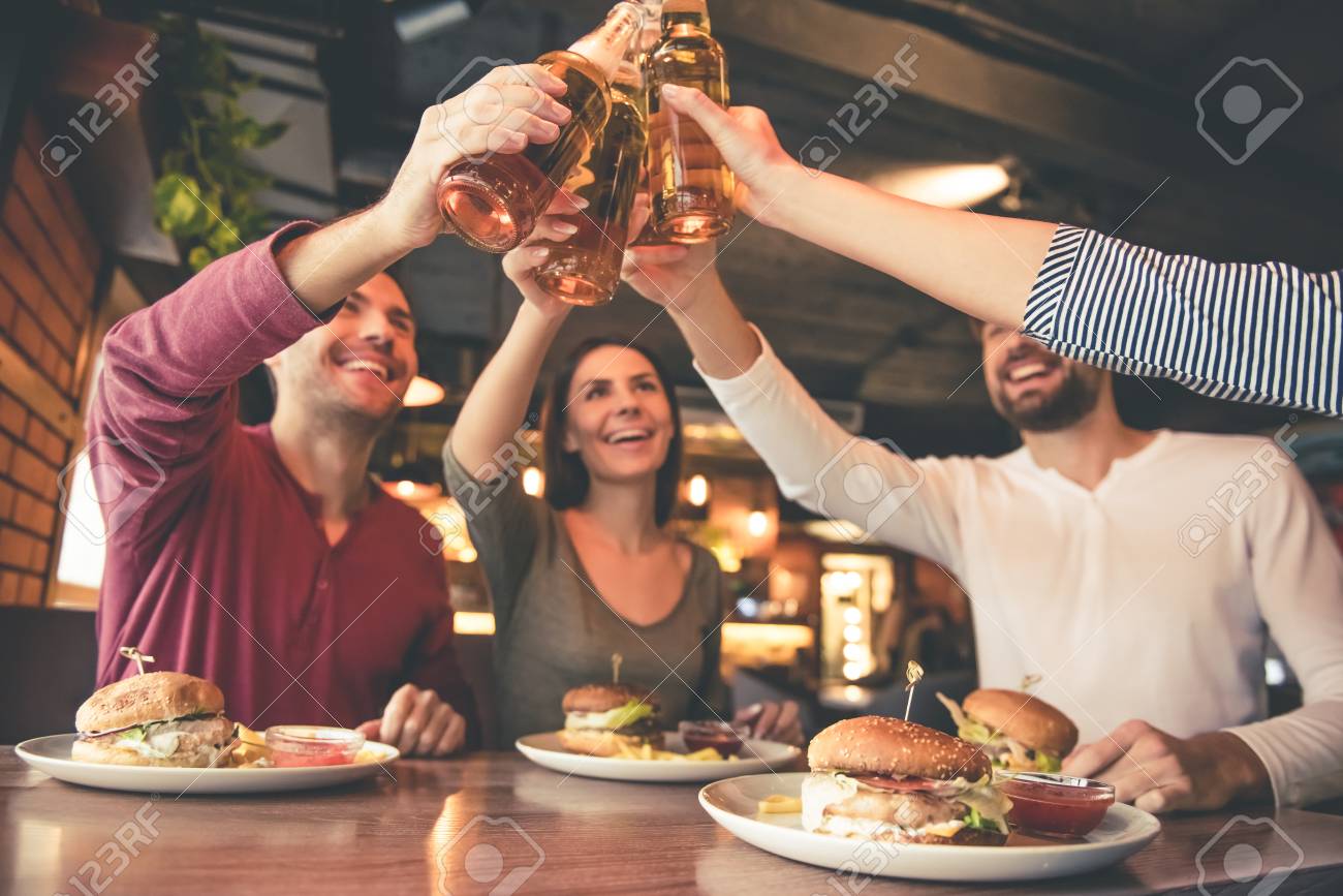 Happy friends are clinking bottles and smiling while spending time together in cafe - 68932907 Happy friends are clinking bottles and smiling while spending time together in cafe - 68932907