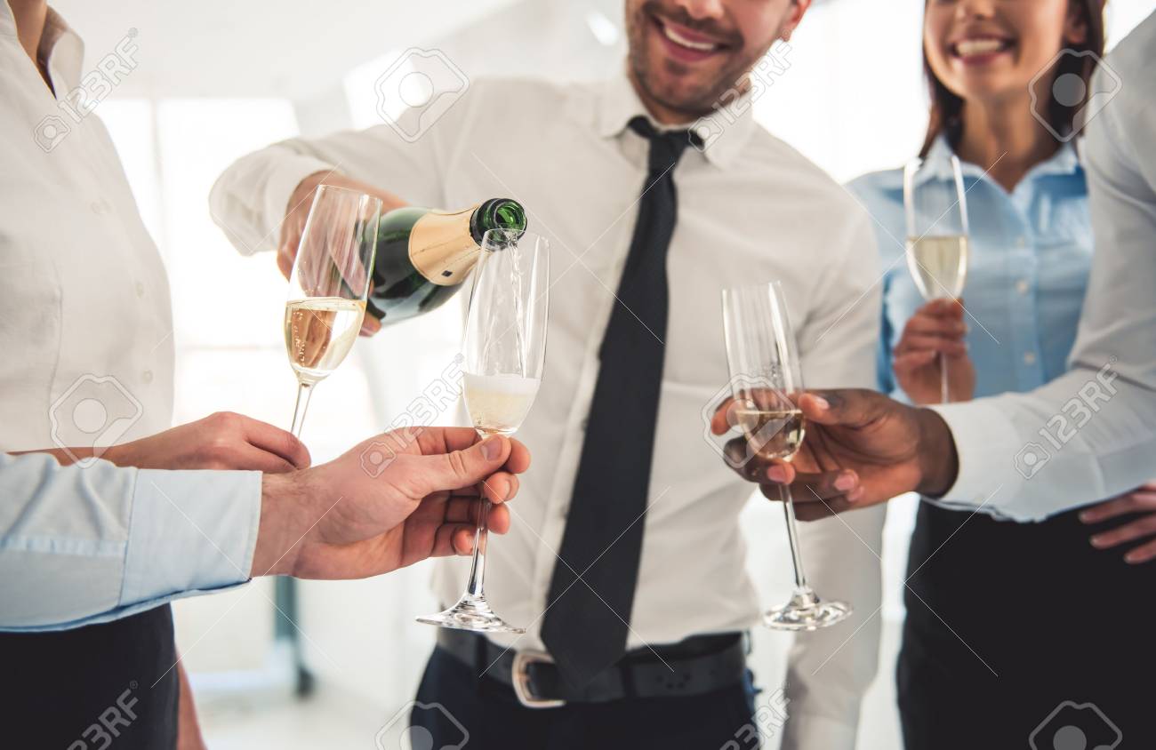 Cropped image of successful business people drinking champagne, talking and smiling while celebrating in office - 71669271 Cropped image of successful business people drinking champagne, talking and smiling while celebrating in office - 71669271