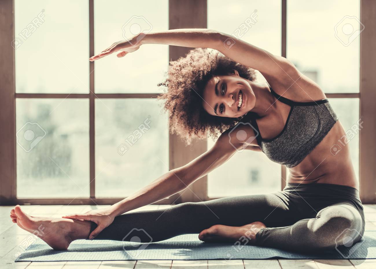 Attractive Afro American girl in sportswear is stretching, looking at camera and smiling - 81369658 Attractive Afro American girl in sportswear is stretching, looking at camera and smiling - 81369658