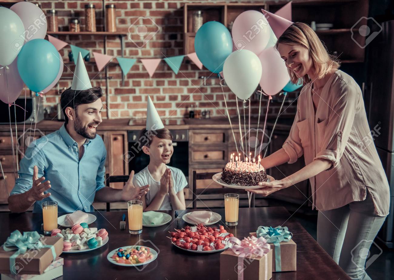 Happy Dad And Son Are Sitting At The Table In Decorated Kitchen