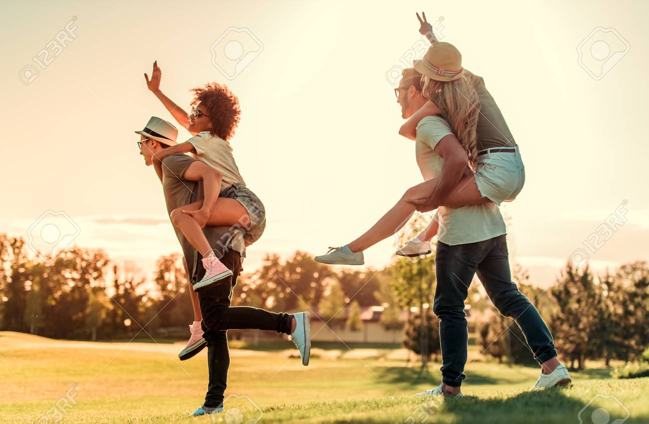 Casais Jovens Felizes Estao Andando E Sorrindo Enquanto Descansava Ao Ar Livre No Tempo Ensolarado As Meninas Estao Sentados Pickaback Fotos Retratos Imagenes Y Fotografia De Archivo Libres De Derecho Image 83498840