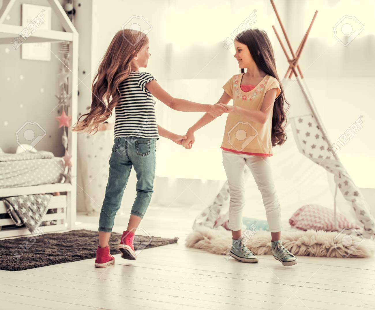 Two happy little girls are dancing and smiling while playing in children's room at home - 84680757 Two happy little girls are dancing and smiling while playing in children's room at home - 84680757