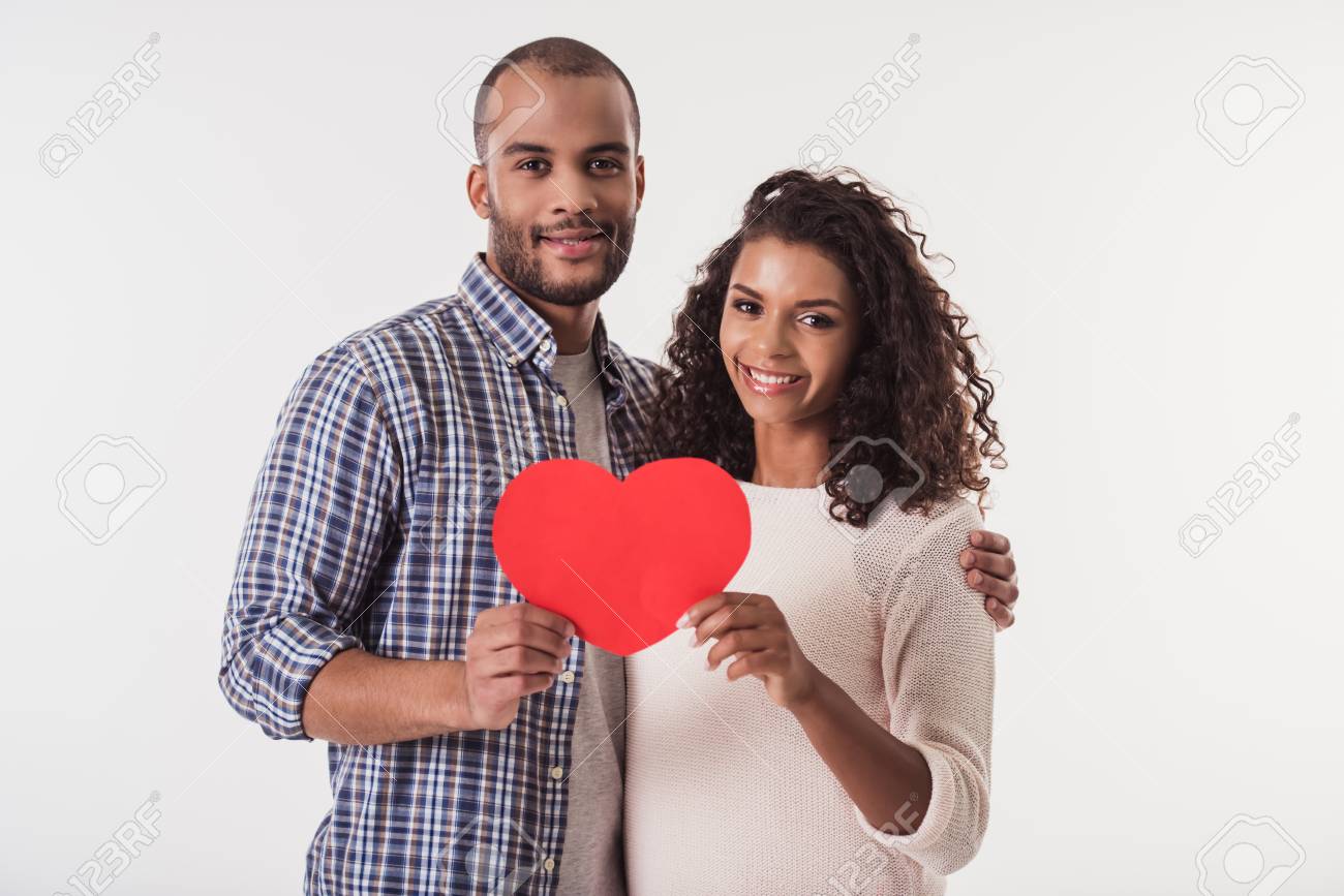 Beautiful Afro American couple holding a big red paper heart, looking at camera and smiling, isolated on white background - 89604185 Beautiful Afro American couple holding a big red paper heart, looking at camera and smiling, isolated on white background - 89604185