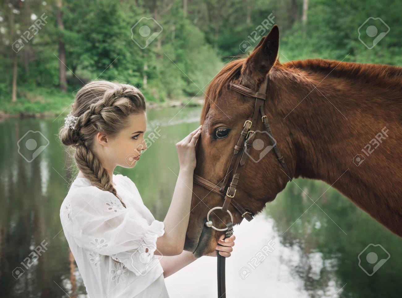 ヴィンテージのドレスに立って湖近くの馬と馬の顔に触れる女性 の写真素材 画像素材 Image