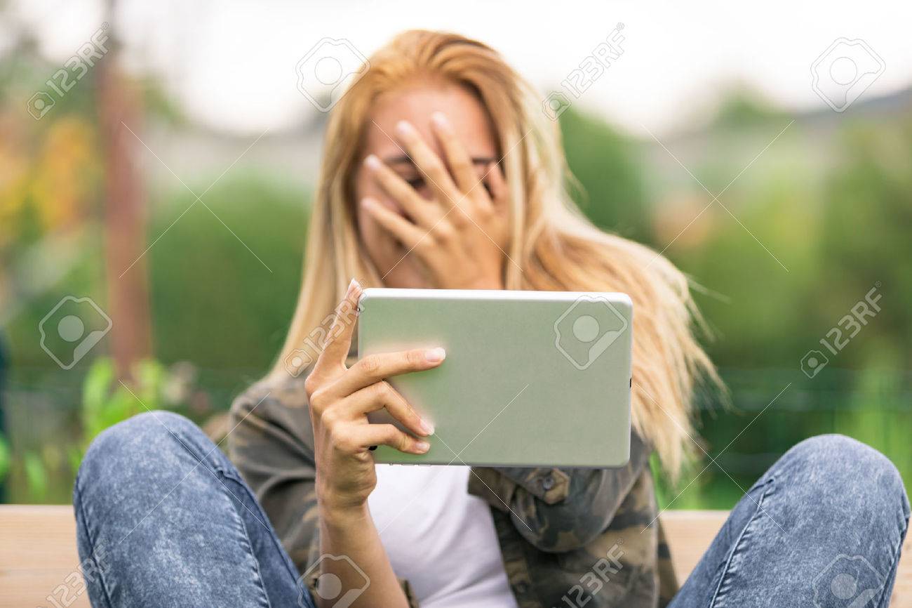 彼女はいくつかのポルノのビデオまたは彼女は彼女のタブレットを屋外で使うインターネットで見た別の禁じられたもので恥ずかしいので 彼の笑顔を隠す若い女 の写真素材 画像素材 Image