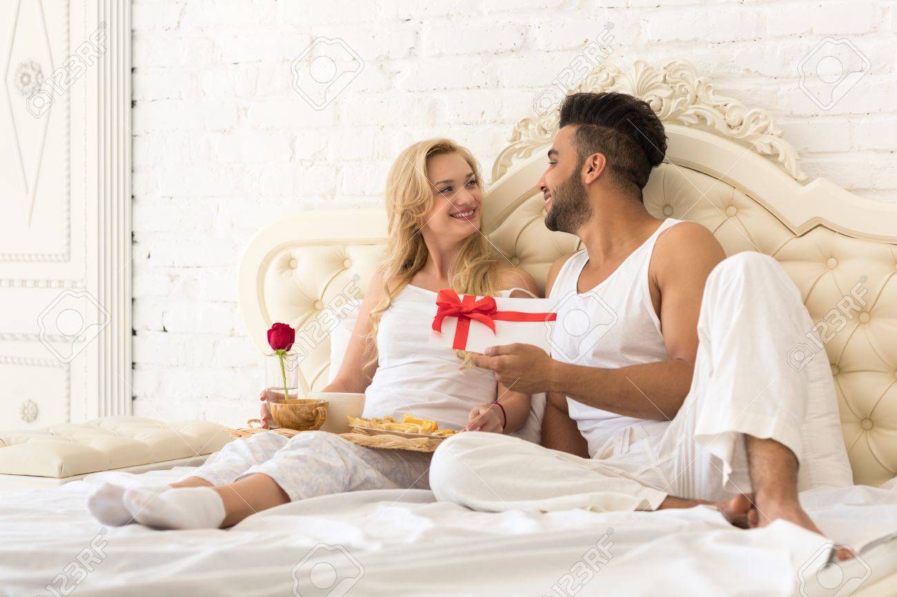 Jeune Couple Heureux Couche Dans Son Lit Homme Hispanique Donner Femme Surprise Enveloppe Present Avec Ruban Anniversaire Celebration Amoureux Dans Chambre Banque D Images Et Photos Libres De Droits Image