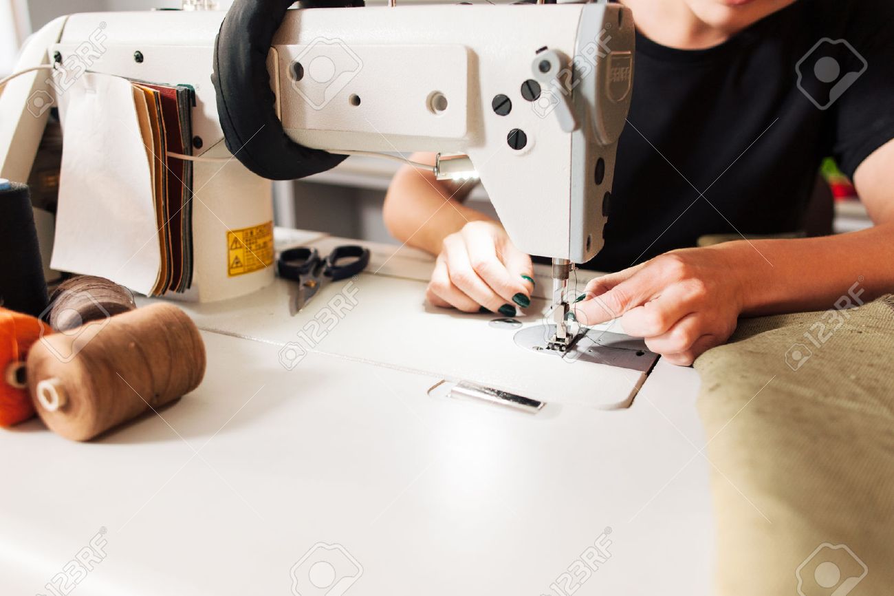 seamstress sews clothes and put thread in needle. Workplace of tailor - sewing machine, rolls of of thread, fabric, scissors. - 52171906 seamstress sews clothes and put thread in needle. Workplace of tailor - sewing machine, rolls of of thread, fabric, scissors. - 52171906