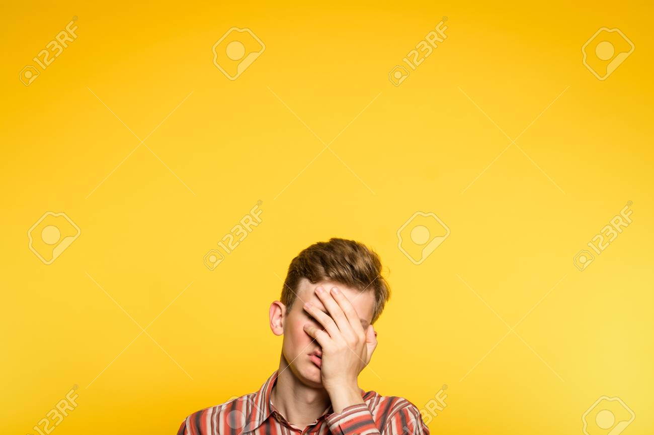facepalm. ashamed abashed man covering his face with hand. portrait of a young guy on yellow background popping up or peeking out from the bottom. copy space for advertising. - 103987168 facepalm. ashamed abashed man covering his face with hand. portrait of a young guy on yellow background popping up or peeking out from the bottom. copy space for advertising. - 103987168