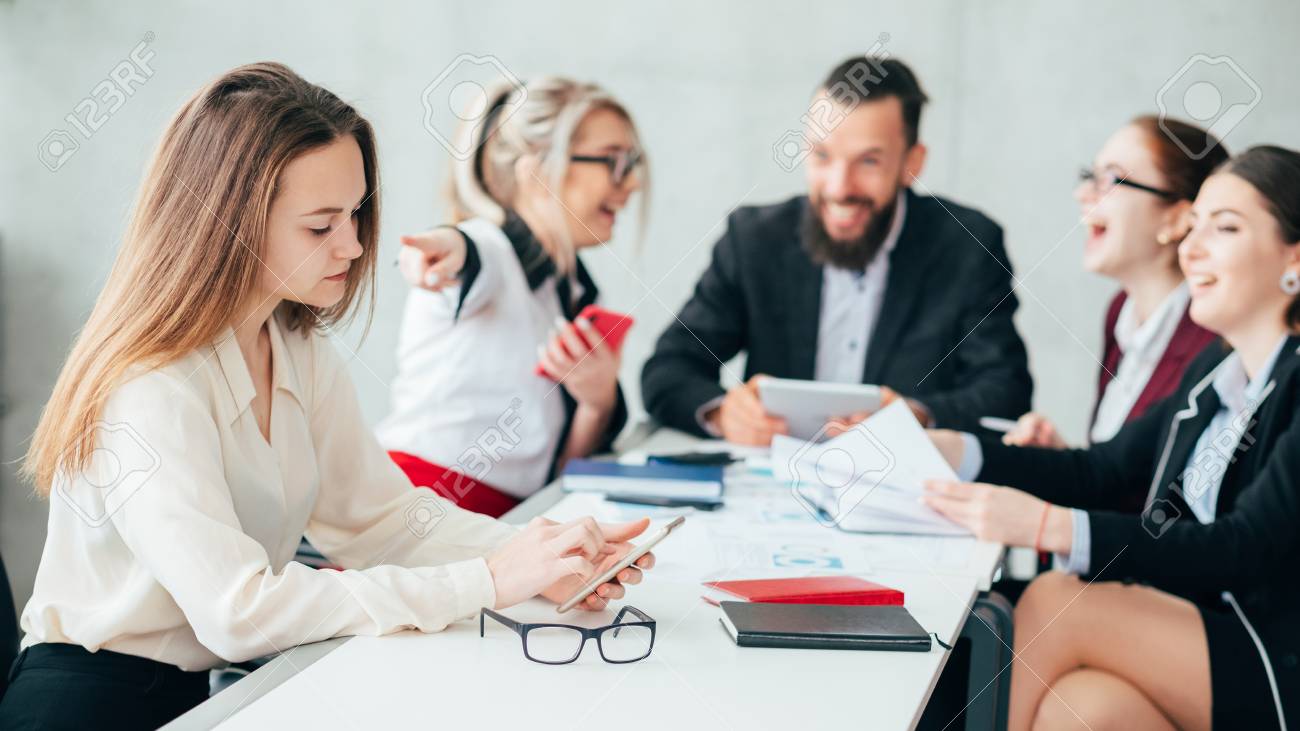 Corporate employees. Bullying and mocking. Business team meeting. Woman point finger at upset colleague checking smartphone. - 117540011 Corporate employees. Bullying and mocking. Business team meeting. Woman point finger at upset colleague checking smartphone. - 117540011