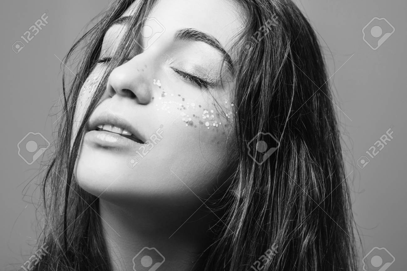 Woman with eyes closed in dreamy relaxation, face tilted upward in soft surrender, glitter dusting her skin like distant stars