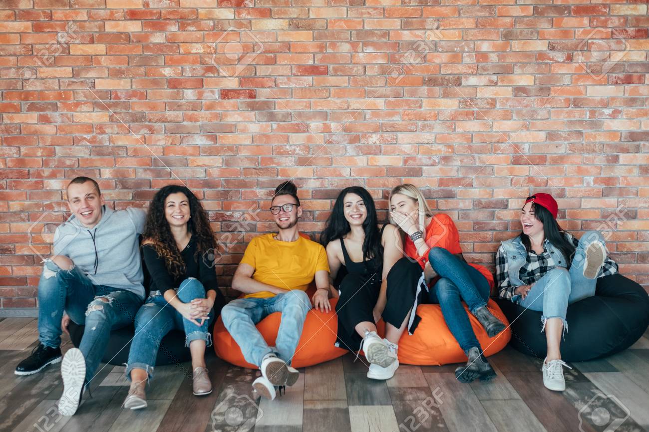 Millennials chilling out in leisure zone after successful hard working day. Young people sitting in cushion chair, laughing. - 121283471 Millennials chilling out in leisure zone after successful hard working day. Young people sitting in cushion chair, laughing. - 121283471