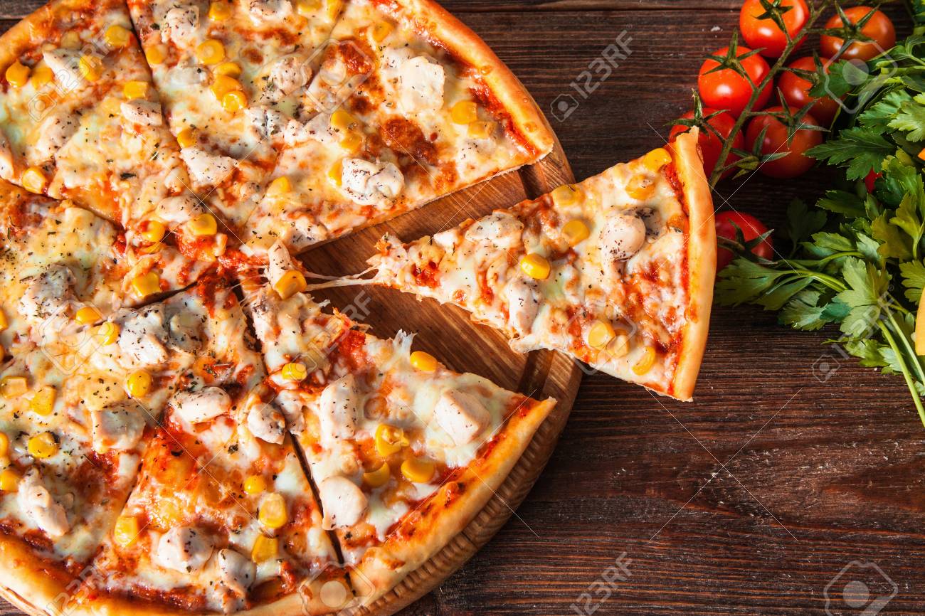 Chaude Pizza Dรฉlicieuse Avec Du Poulet, Du Fromage Et Du Maรฏs Avec Des Morceaux Coupรฉs Servi Sur Une Table En Bois Rustique Avec Des Ingrรฉdients, Poser ร Plat. Nourriture Italienne. Banque D'Images