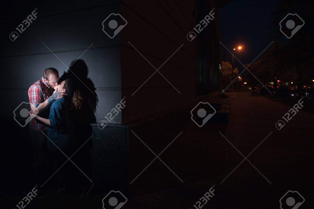 Couple in heated embrace in dark alley shadows, intense forbidden passion