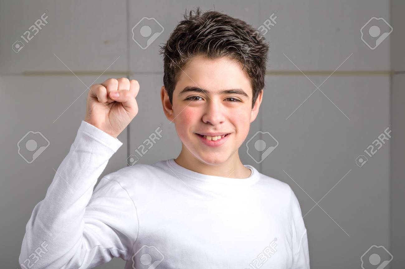 電力産業の背景に彼の右拳を上げるジェスチャーを作る白の長袖 T シャツの笑顔でラテン語の滑らかな肌の少年 の写真素材 画像素材 Image