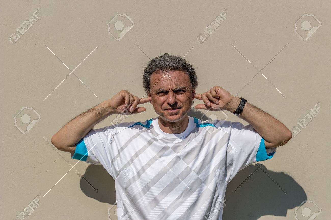 音や言葉を聞いていない指で耳を塞ぐスポーツ T シャツに身を包んだ塩コショウ髪のハンサムな中年男 彼は非常に邪魔です の写真素材 画像素材 Image