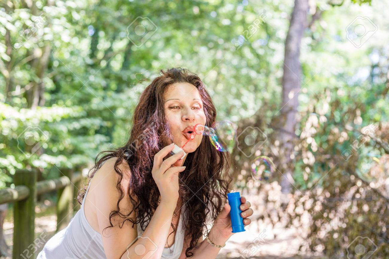 公共の公園でシャボン玉を吹く少女のような魅力的な成熟した大人の女性が楽しんでください の写真素材 画像素材 Image