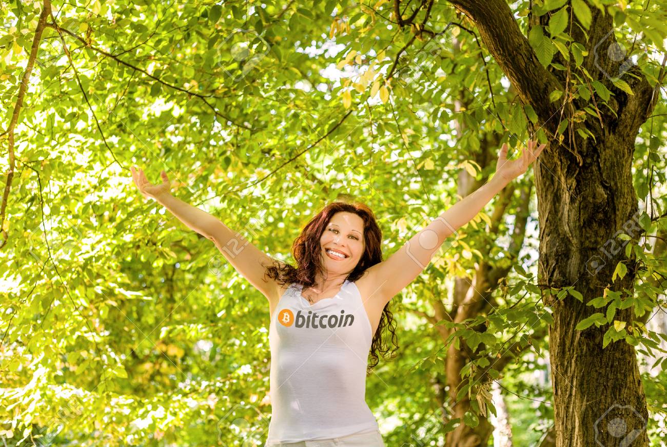 幸せな女性は、パブリックドメインビットコインのロゴを持つタンクトップを着て庭で空に彼女の腕を上げ、喜んで新しい通貨で生活を送りますの写真素材・画像素材  Image 92429369