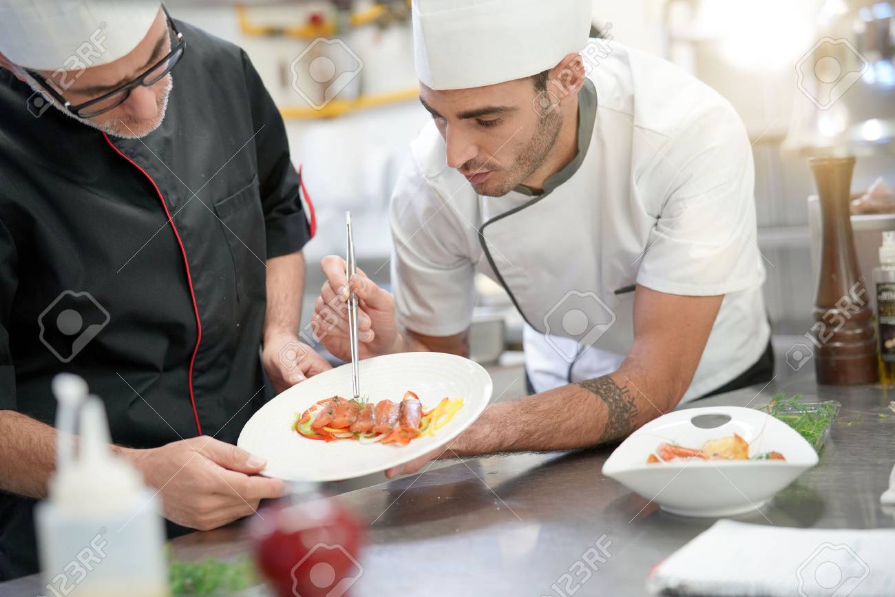 professional cook chefs in kitchen improving dish composition stock