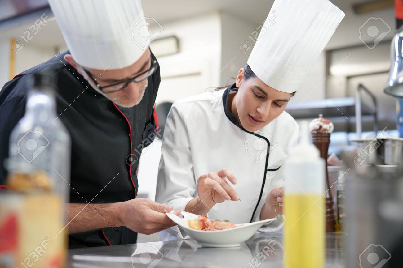 professional cook chefs in kitchen improving dish composition stock