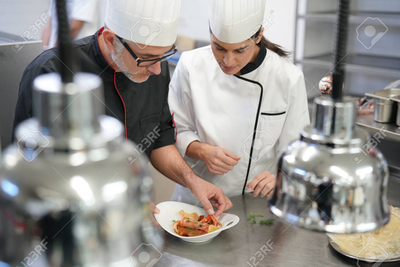 professional cook chefs in kitchen improving dish composition stock