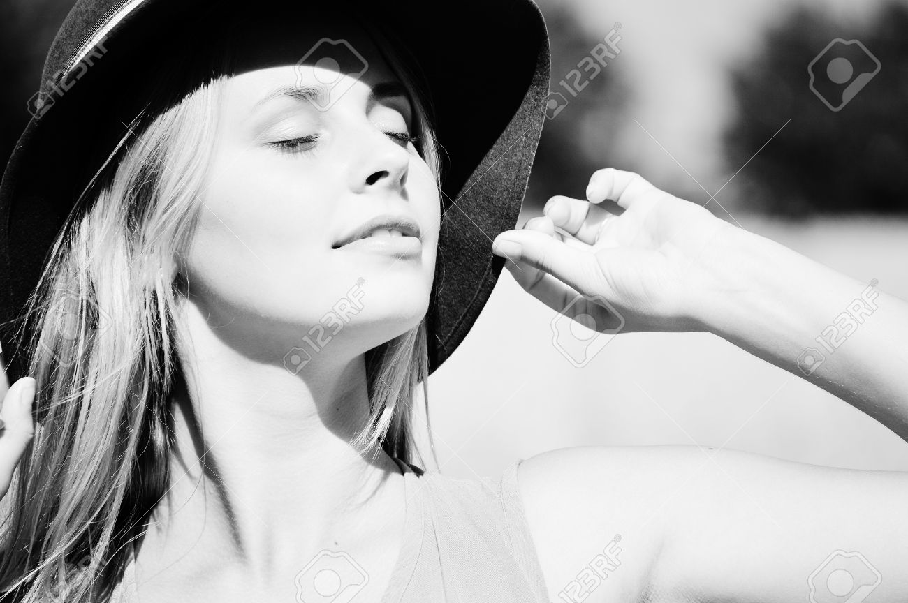 Black and white photography of young sensual lady wearing hat touching it with her hand exposing