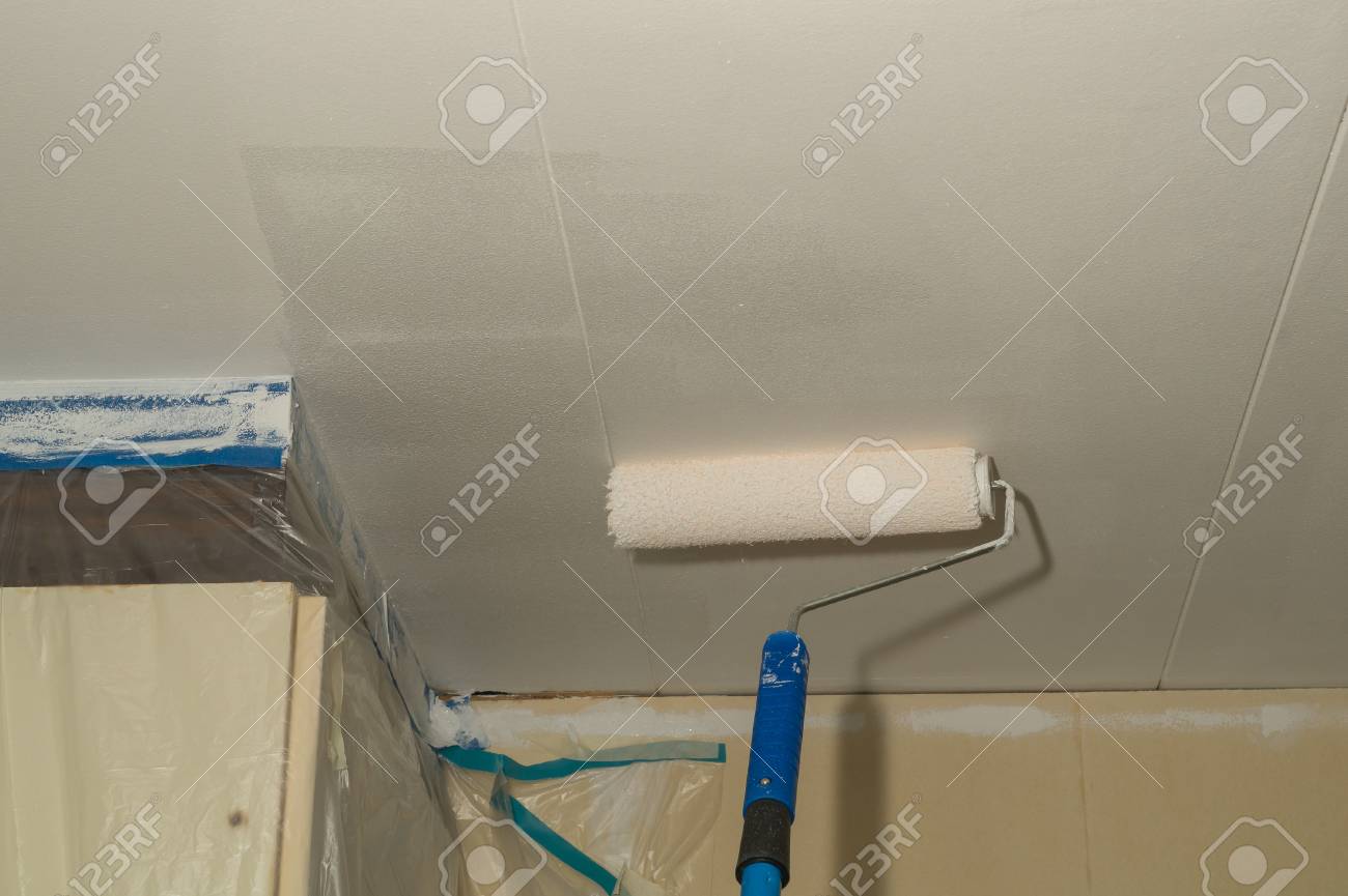 A Man Is Painting The Ceiling White With A Paint Roller Stock
