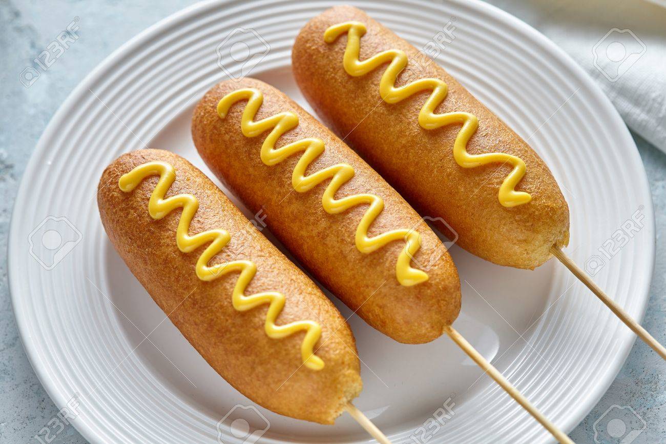 トウモロコシの犬伝統的なアメリカ Corndog 通りジャンク フード ホットドッグ ソーセージ マスタードのスナックと扱うスティック素朴なテーブルで食べる不健康な上にコーンミールの打者の厚い層でコーティング の写真素材 画像素材 Image
