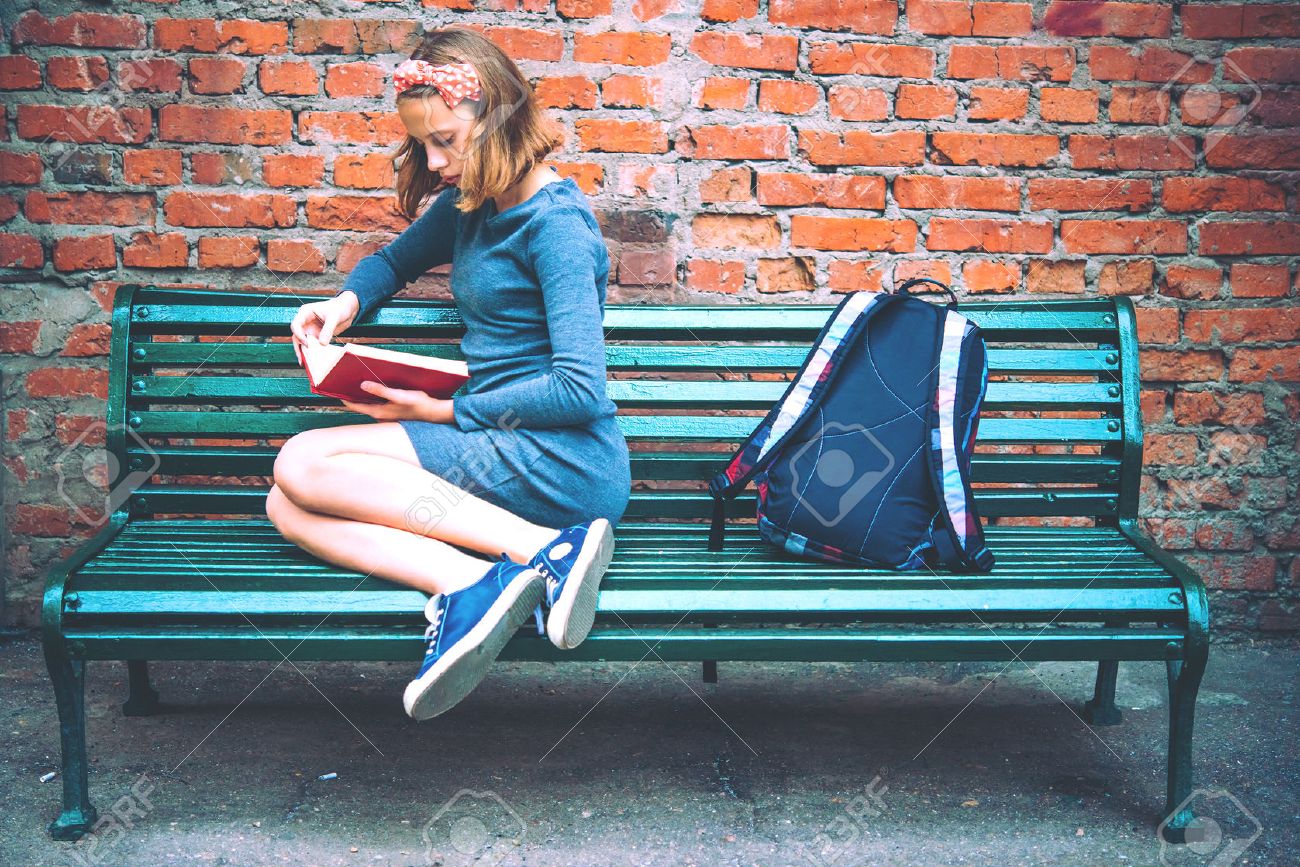 A teenage girl is reading on a bench with brick wall in the background. Toned image - 50840812 A teenage girl is reading on a bench with brick wall in the background. Toned image - 50840812