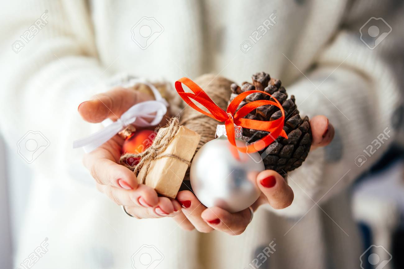 Woman's hands hold christmas or new year decoration. Small gift box, glass ball and cone - 50646068 Woman's hands hold christmas or new year decoration. Small gift box, glass ball and cone - 50646068