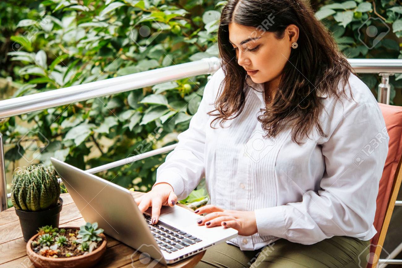 Portrait of beautiful plus size girl working on her laptop on balcony or terrace of cafe - 73658075 Portrait of beautiful plus size girl working on her laptop on balcony or terrace of cafe - 73658075