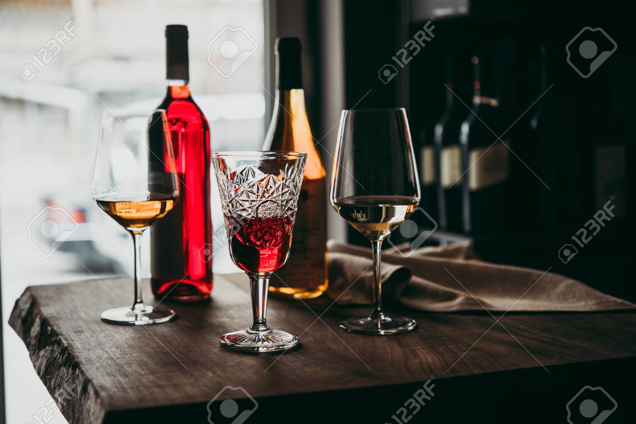 Different glasses and bottles of wine served on a wooden table in a bar or a wine shop. - 103759200 Different glasses and bottles of wine served on a wooden table in a bar or a wine shop. - 103759200