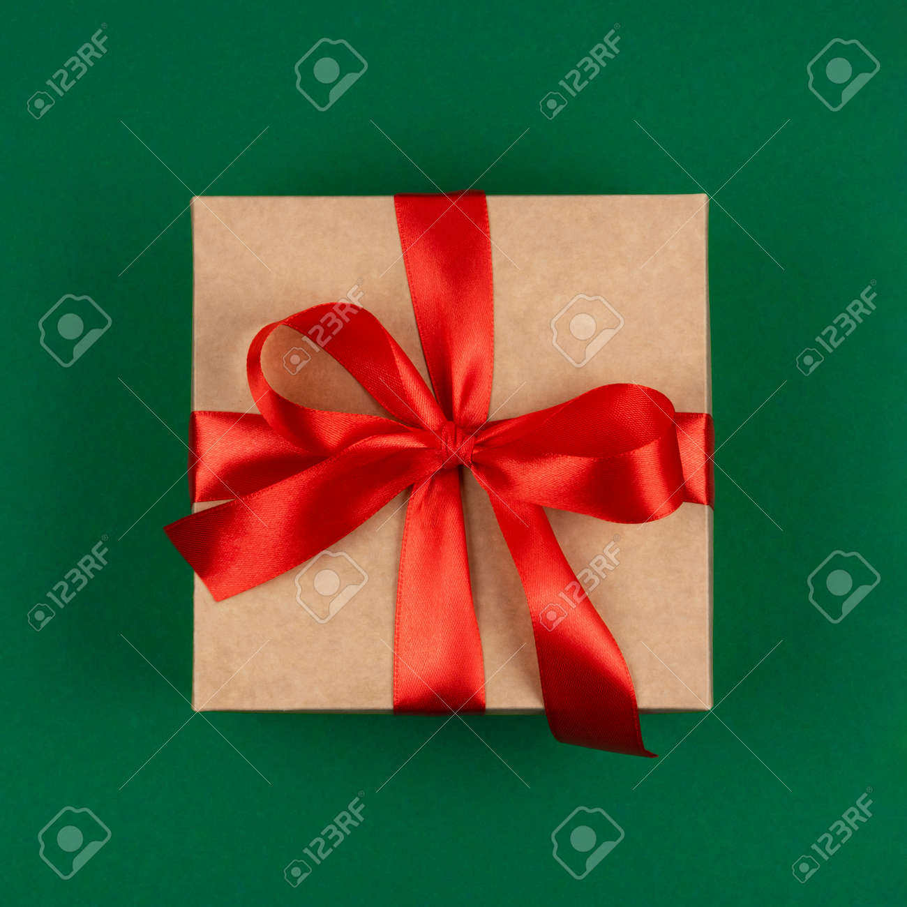 Top view of craft Merry Christmas gift with red bow ribbon over green background. Happy New Year greetings. Festive winter holidays backdrop. Flat lay. Happy Birthday card. - 158170698 Top view of craft Merry Christmas gift with red bow ribbon over green background. Happy New Year greetings. Festive winter holidays backdrop. Flat lay. Happy Birthday card. - 158170698