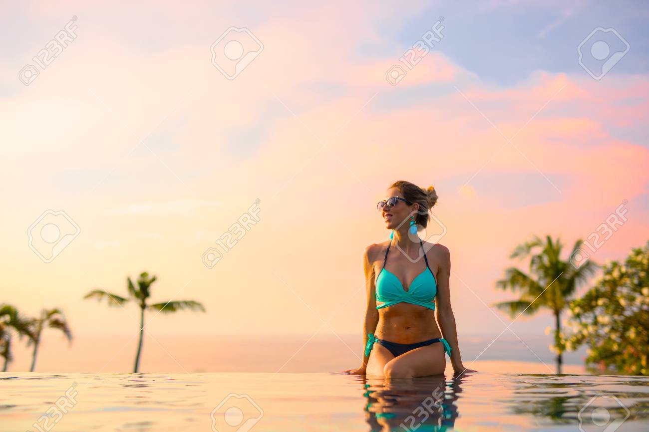 Girl sitting on edge of infinity pool at beautiful sunset - 91381780 Girl sitting on edge of infinity pool at beautiful sunset - 91381780