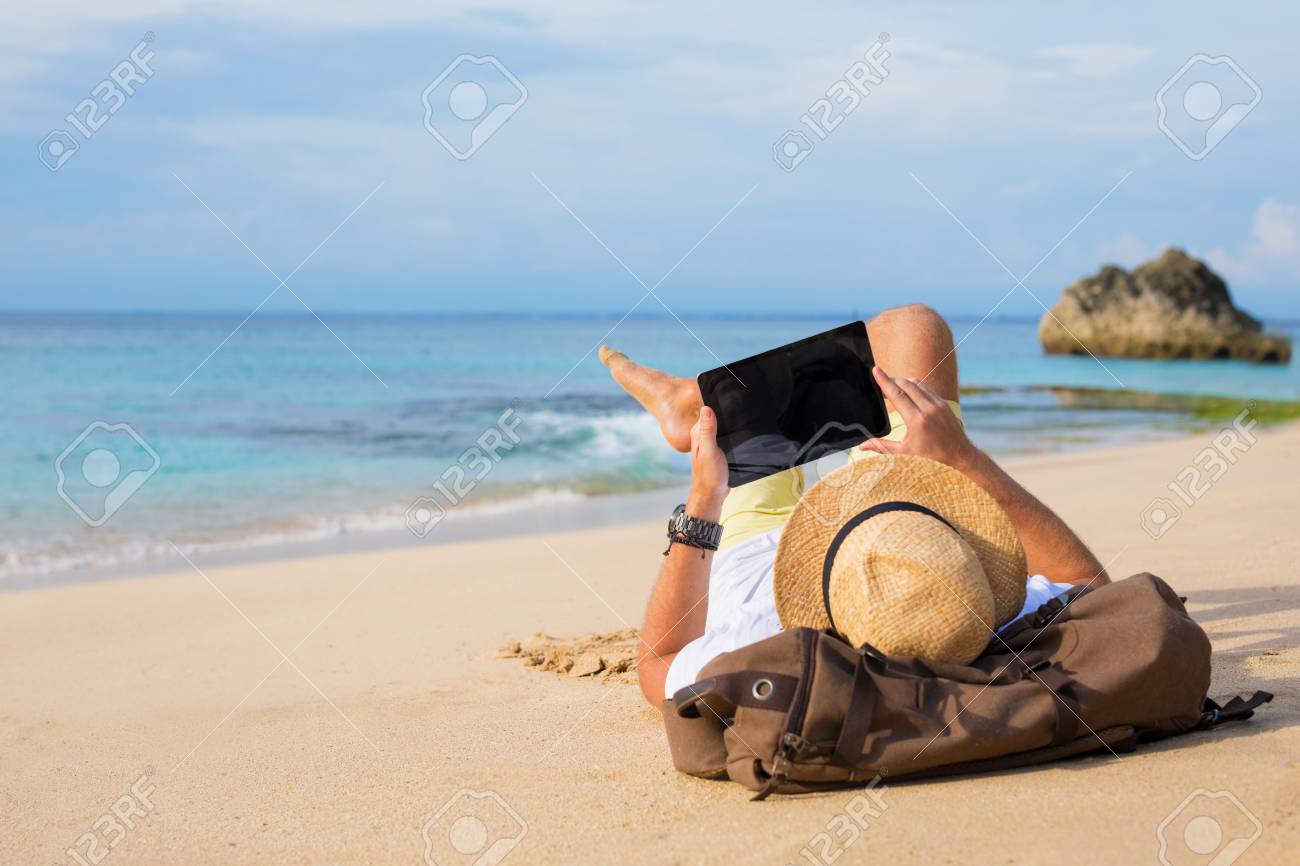 Man lying on the beach and using tablet - 99564114 Man lying on the beach and using tablet - 99564114