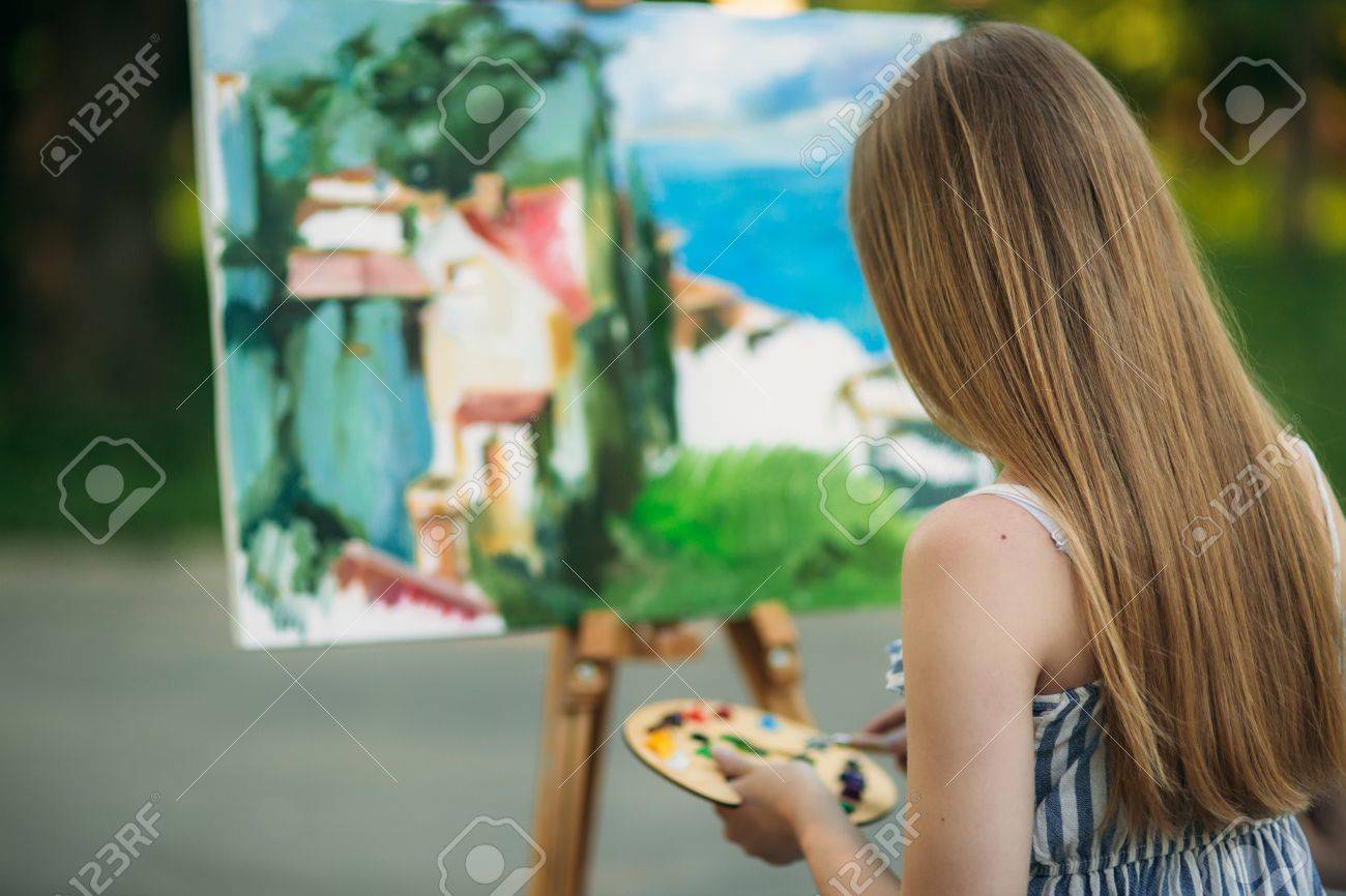 ブロンドの女の子は 塗料の助けを借りて キャンバスに絵を描きます 木製のイーゼルは 画像を保持します 夏 の写真素材 画像素材 Image